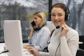 Image of lady answering the phone using a headset, facing the camera and smiling, with the hand closest to the camera holding the microphone stem of the headset